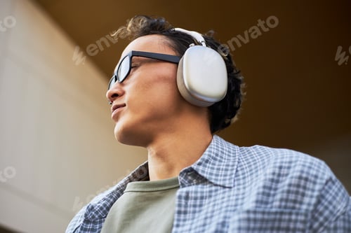 Preview: Young Adult Asian Man Listening to Music with Headphones Outdoors