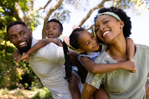 Preview: African american playful parents piggybacking happy daughter and son while standing in playground