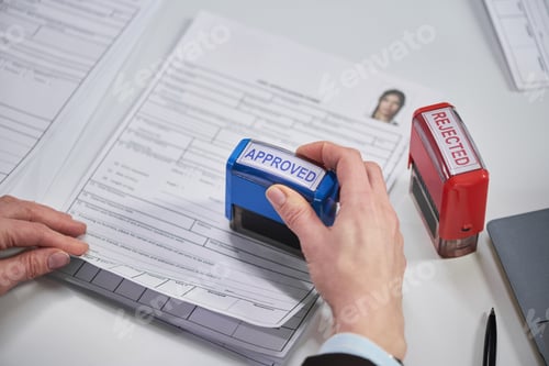 Preview: Female Hand Stamping Approved on Visa Application Documents at Desk