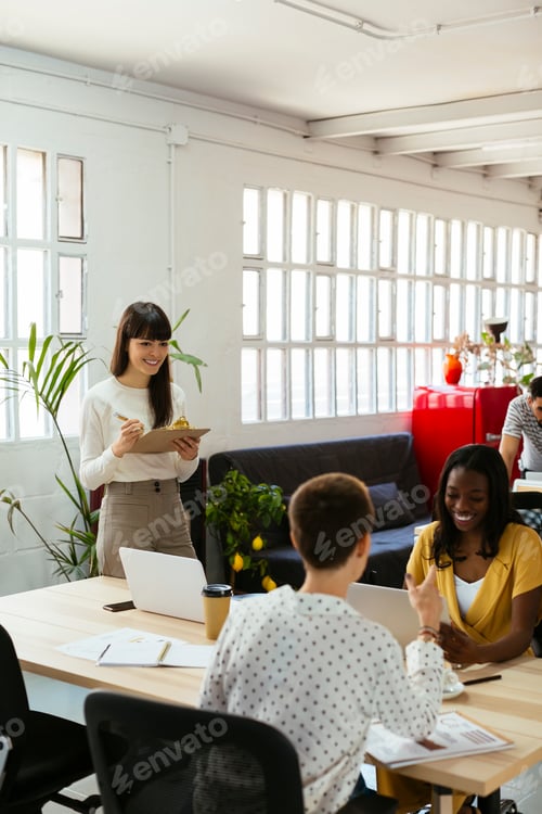 Preview: Smiling woman with clipboard among colleagues in office