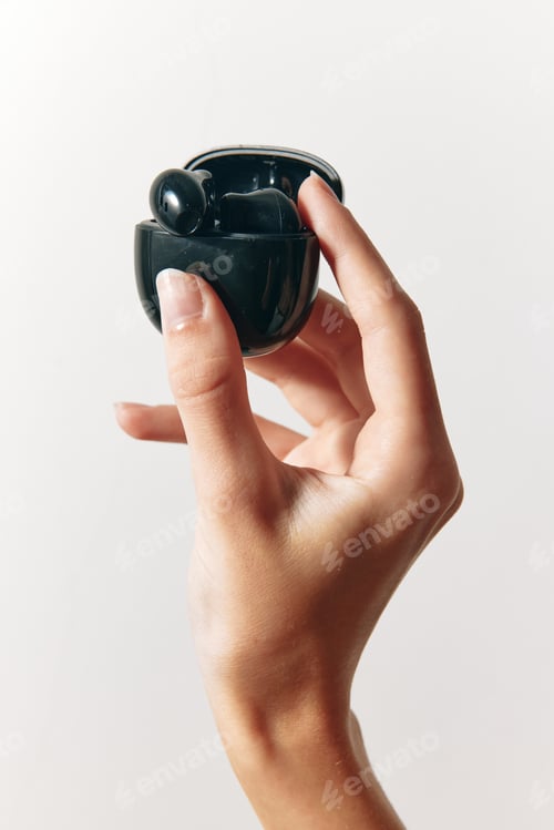 Preview: Person holding a small black earbud in their hand, with finger and thumb touching the top and bottom