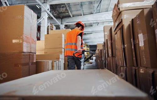 Preview: Young male worker in uniform is in the warehouse pushing pallet truck