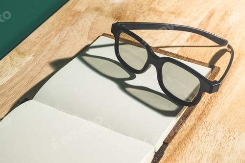 Preview: Close up black eyeglasses on open blank book with shadow light from window
