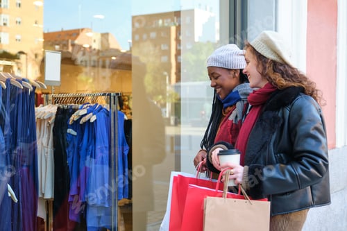 Preview: Two multiracial female friends looking at shop window in the city.