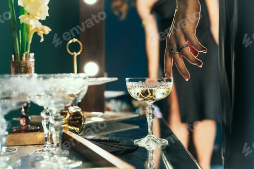 Preview: Crystal glass with champagne standing on the table. Tender female hand stroking glass. Bar and drink