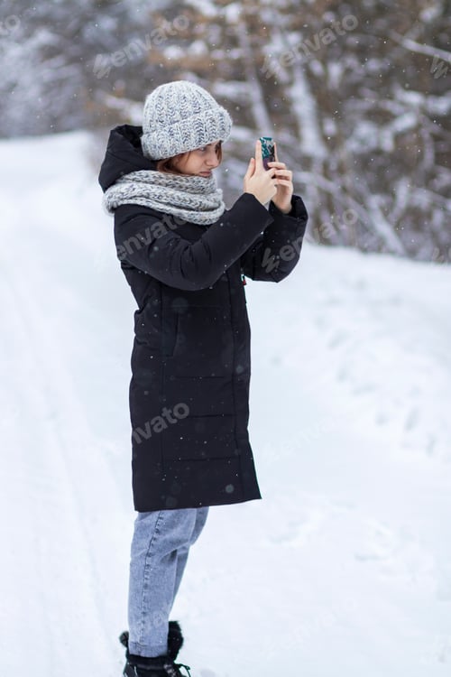 Preview: Girl with a smartphone in her hand, in the winter forest