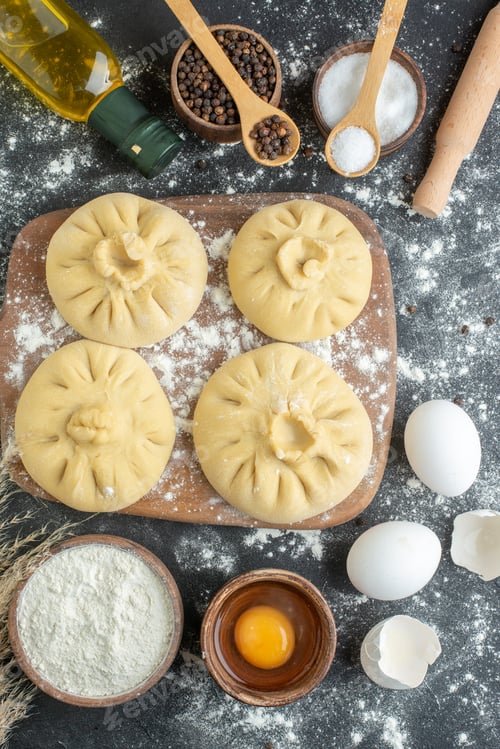 Preview: top view raw dumplings on cutting board with flour and eggs on dark background dough horizontal