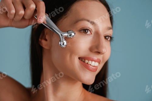 Preview: Silver colored facial massager. Young woman is in the studio against background