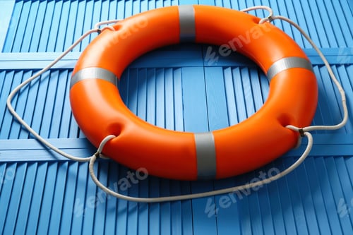 Preview: Orange lifebuoy on blue wooden background, closeup. Rescue equipment