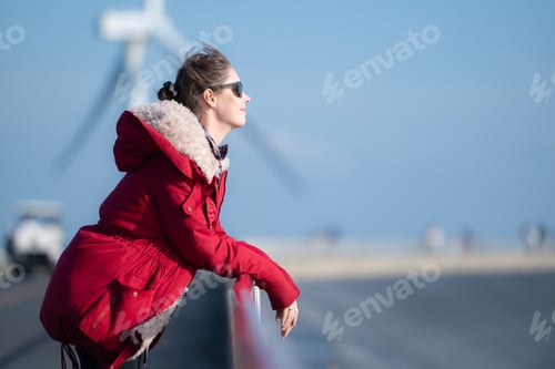 Preview: On the background of windmills, A young woman in a red jacket is enjoying her winter vacation.