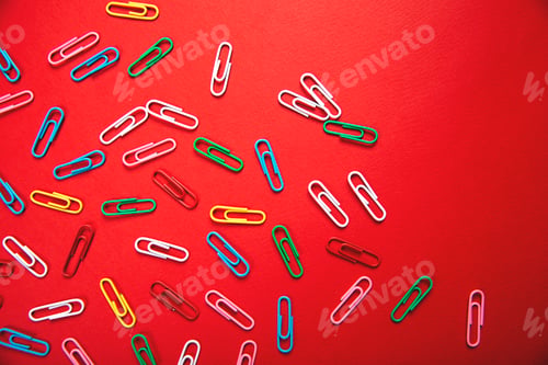 Preview: A lot of colorful paper clips lie on an red background.