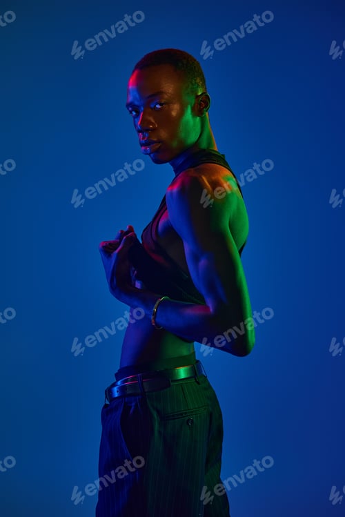 Preview: Vibrant young man showcasing stylish attire in a colorful lit studio setting