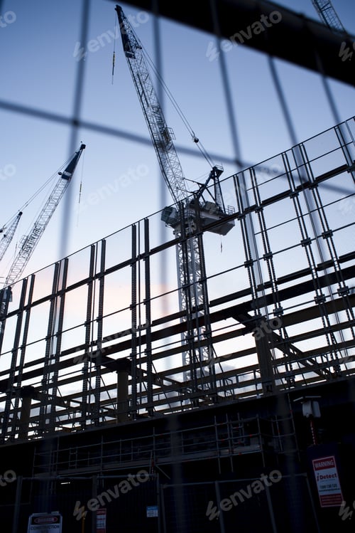 Preview: Vertical low angle shot of cranes in the process of construction of a building under evening sky