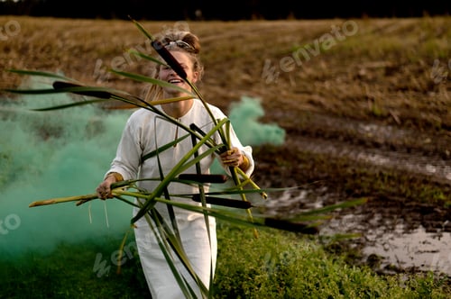 Preview: Happy woman in white dress with smoke bomb and reeds dancing on muddy field