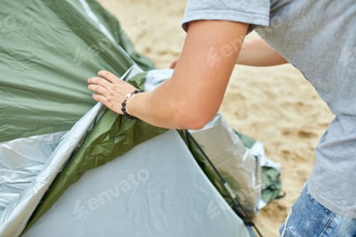 Preview: Young male tourist puts a green tent in the beach coast . The man sets up a camp on a hike