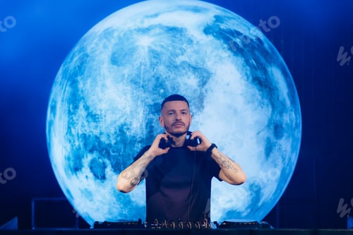 Preview: DJ Performing in Front of Large Moon Projection at Night Event