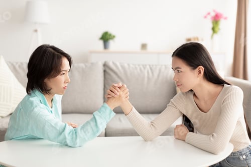 Preview: Mature Asian mother and adult daughter arm wrestling, looking each other in eyes, fighting at home