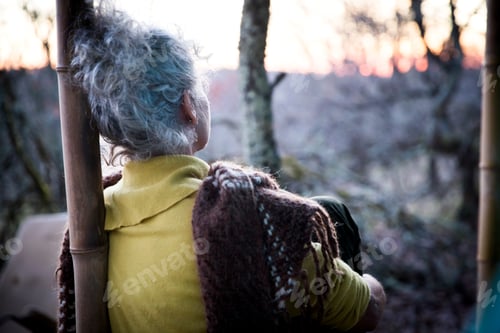 Preview: Rear view of mature woman sitting on woodland porch watching sunset