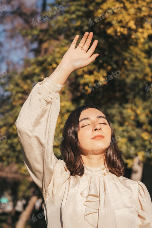 Preview: Young Hispanic woman with eyes closed enjoying sunlight in a park