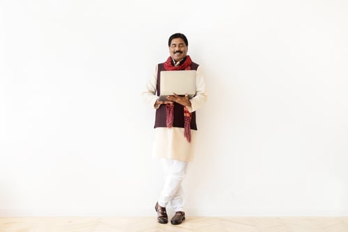 Preview: Positive middle aged indian man using laptop on white background