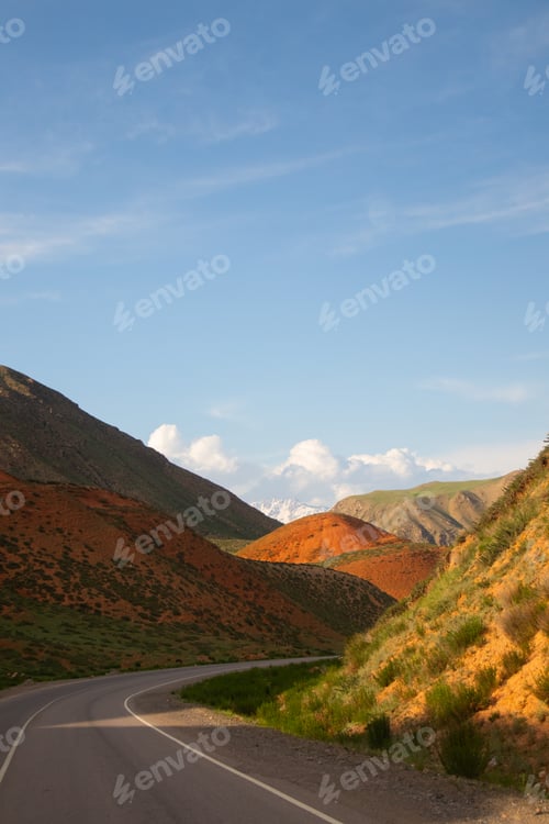 Preview: Road curving through orange and green mountains with snow peaks in distance