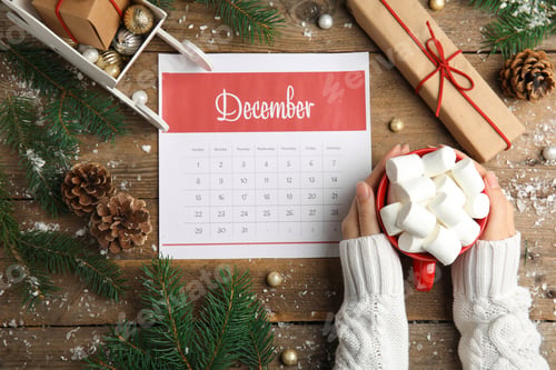 Preview: Woman holding hot drink near paper calendar at wooden table, top view