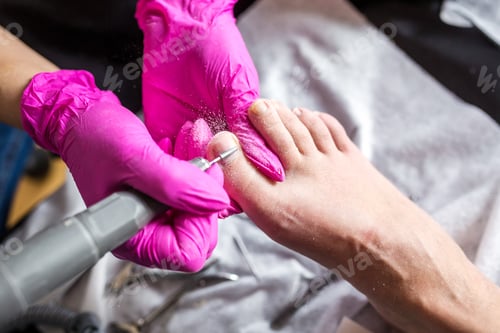 Preview: Pedicurist master in pink gloves cuts the cuticle and shellac toe nails in the pedicure salon