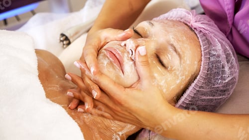 Preview: Cosmetologist applies a moisturizing mask on female face. Woman in a spa salon, cosmetic procedures