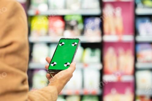 Preview: Hand of young female shopaholic holding smartphone with green e-coupon