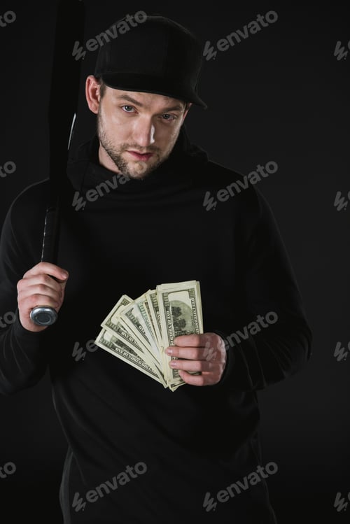 Aperçu: young robber in zoodie with baseball bat and money isolated on black