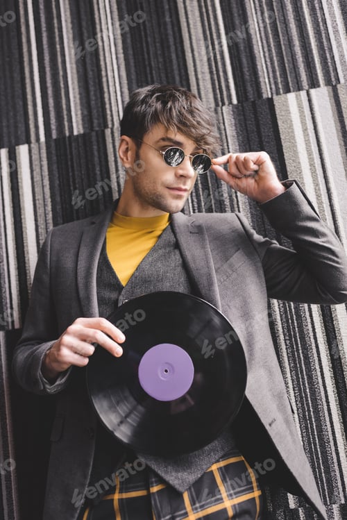 Preview: cheerful young man touching sunglasses and holding plastic retro vinyl record