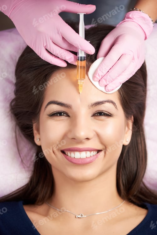 Preview: Smiling woman getting injection for female forehead face in the cosmetology salon.