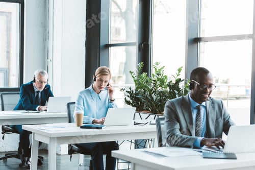 Preview: multiethnic professional business people in headsets using laptops in modern office