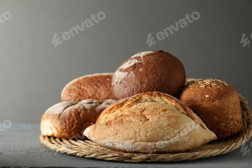 Preview: Wicker basket with different types of fresh bread on grey wooden table, closeup
