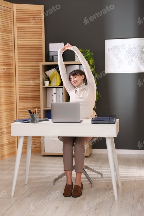 Preview: Young businesswoman stretching her arms and back at table in office
