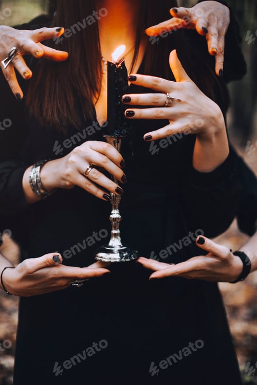 Preview: Witch with burning candle being touched by many hands during magic ritual in dark autumn forest