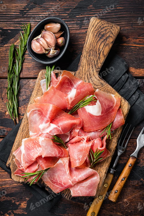 Preview: Slices of jamon serrano ham or prosciutto crudo parma on wooden board with rosemary.