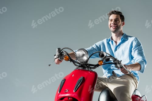 Preview: portrait of happy fashionable young man riding red scooter isolated on grey