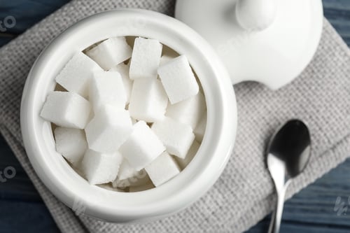 Preview: Refined sugar cubes in ceramic bowl on blue wooden table, top view