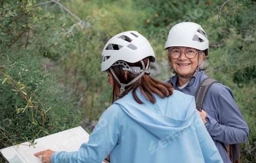 Preview: Senior women hikers with helmets standing on the top of mountain looking at map