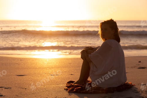 Preview: Beautiful woman sitting on the beach during sunset