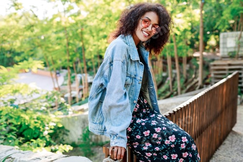 Preview: Smiling woman with Afro hairstyle sitting on a fence in summer sunny park