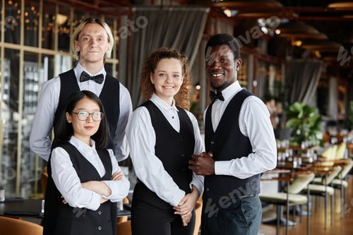 Preview: Diverse group of servers wearing classic tuxedo uniform smiling at camera