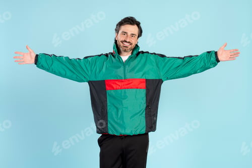 Vista previa: Happy man opening arms wearing 90s style jacket on blue background