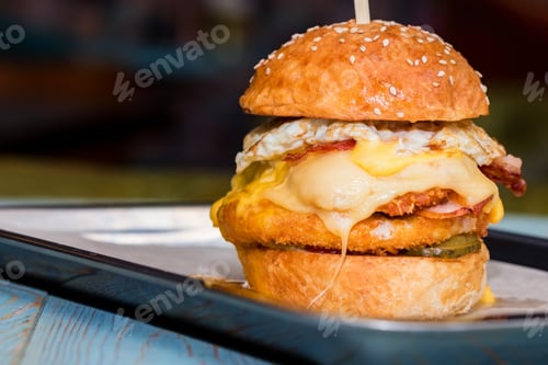 Preview: Close up tall tasty burger with cheese and egg served on tray
