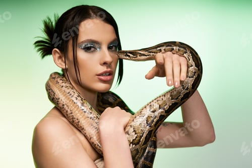 Preview: Captivating pose of a young woman gracefully interacting with a snake in a striking setting