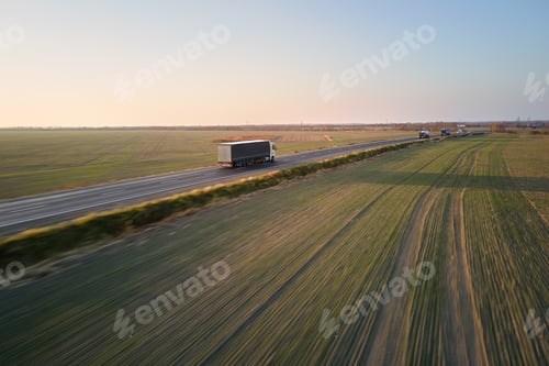 Preview: Aerial view of semi-truck with cargo trailer driving on highway hauling goods in evening.