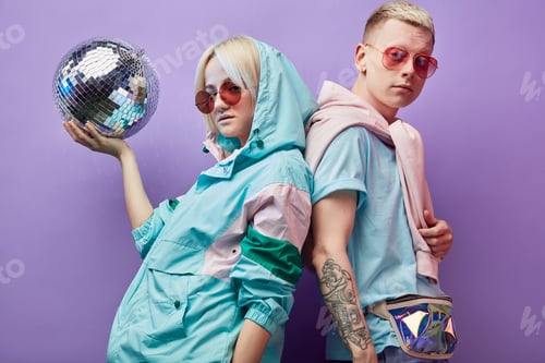 Preview: Young fashionable couple of dancers posing with disco ball on violet background