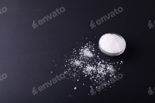 Preview: High angle view of salt in dish and fallen on black table with copy space