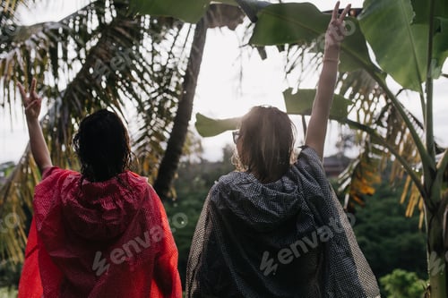 Preview: Two girls in raincoats walking around jungle. Female travelers having fun during journey to Indones